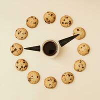 Clock made of cup of coffee, black waffle ice cream cone and chocolate cookies on cream background. Creative food concept. Minimal coffee and biscuits idea. Yummy chip cookies composition. Flat lay. photo