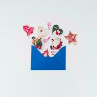 Creative composition made of various Christmas objects coming out of blue envelope on white background. Minimal Christmas or New Year concept. Trendy winter holidays idea. Flat lay, top of view. photo