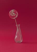 Lollipop as a flower in a vase against red background. Summer candy concept. Creative sweet idea. photo