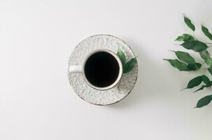 Creative concept made of coffee cup and green leaves on white background. Flat lay, top view. Minimal layout. photo