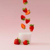 Creative layout made of strawberries falling into glass cup of milk drink with strawberry taste on pastel pink background. Minimal smoothie or milkshake concept. Healthy food for breakfast and snack. photo