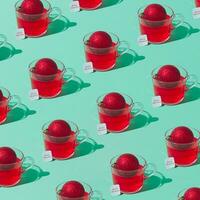 Christmas pattern composition of transparent glass cup of fruit tea with teabag made of red Christmas bauble on green background. Minimal Christmas or New Year concept. Trendy winter holidays idea. photo