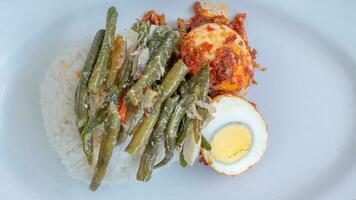 A plate of rice with egg balado and long bean sauce, chili sauce filled with eggs, anchovies and tofu. Served in a bowl on a gray background. Selected focus. photo