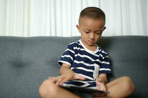 Asian boy uses tablet to watch video clips on sofa in home photo