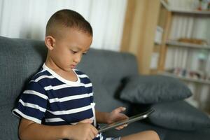 Asian boy uses tablet to watch video clips on sofa in home photo