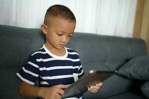 Asian boy uses tablet to watch video clips on sofa in home photo