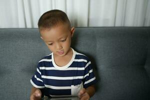 Asian boy uses tablet to watch video clips on sofa in home photo