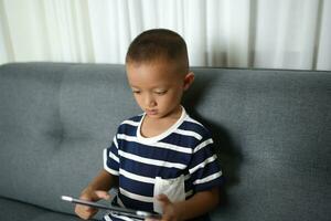 Asian boy uses tablet to watch video clips on sofa in home photo