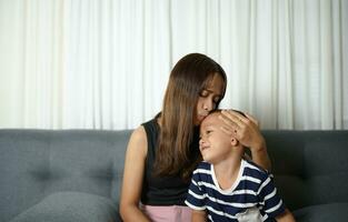 Mother kisses Asian boy on sofa in house photo