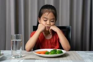 Little cute kid girl refusing to eat healthy vegetables. Children do not like to eat vegetables. photo
