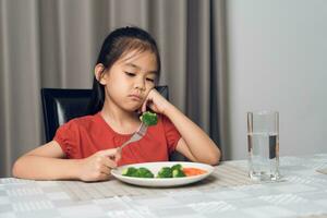 Little cute kid girl refusing to eat healthy vegetables. Children do not like to eat vegetables. photo