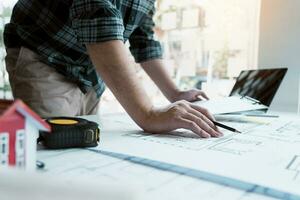 diseñador de interiores o arquitecto revisando planos y sosteniendo dibujos a lápiz en el escritorio de la oficina en casa. foto