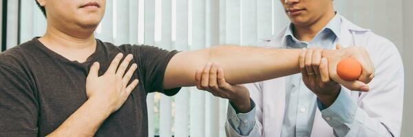 Asian young male physiotherapist helping patient with lifting dumbbells exercises in clinic. photo