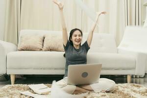 Asian woman throws papers in the living room as she finishes her work with her laptop on her lap. photo