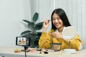 Beautiful asian woman blogger using camera phone recording vlog video live streaming and showing how to make up cosmetics at home. photo