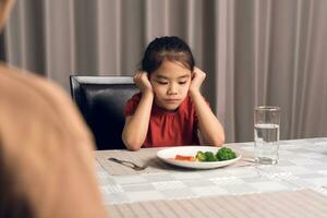 Mother is telling her cute kid eat useful vegetables but the child refuses to eat. photo