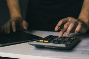 Asian man is using a calculator to calculate his monthly miscellaneous expenses at home. photo