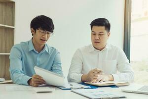 Two businessmen are analyzing company earnings figures at their desks. photo