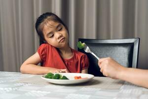 Little cute kid girl refusing to eat healthy vegetables. Children do not like to eat vegetables. photo