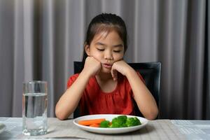 Little cute kid girl refusing to eat healthy vegetables. Children do not like to eat vegetables. photo