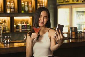 mujer asiática tomándose una foto mientras bebe whisky en el bar.