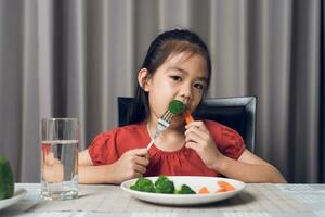 Asian little girl eating healthy vegetables with relish. photo