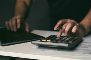 Asian man is using a calculator to calculate his monthly miscellaneous expenses at home. photo