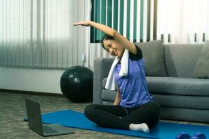 Asian woman stretching during a yoga class with a trainer at her laptop computer at home. photo