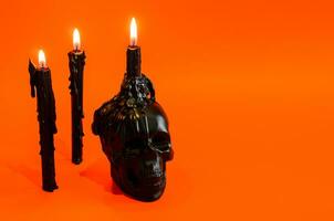 Black skull and candles with flame put on orange background. Halloween party concept. photo