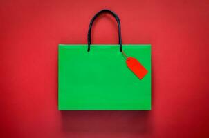 Green shopping paper bag with red blank price tag on red background for Black Friday shopping sale concept. photo