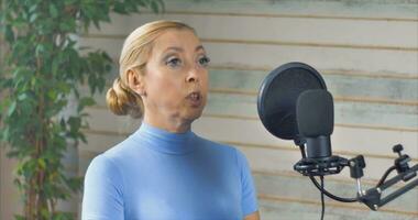 une fille avec bleu yeux et une bleu col roulé conduit une Podcast avec une grand microphone video