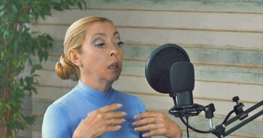 A girl with blue eyes and a blue turtleneck conducts a podcast with a microphone video