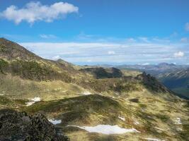 Bright sunny atmospheric scenery on top of spotted mountain ridge under white clouds and blue sky. Beautiful landscape above mountain range with sunlight. Western Sayans. photo