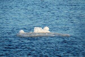 White iceberg of the remnants of ice floats on the blue water. The ice melts in the spring. Natural background. photo