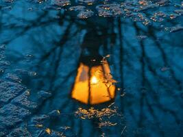 Blurred antique lantern shines yellow and is reflected in a spring puddle. Urban postcard abstract view. photo