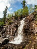 Scenic summer landscape with vertical big waterfall at mountain top in sunshine in the Ergaki Park. Russia, West Sayans. High falling water in Siberia region. photo