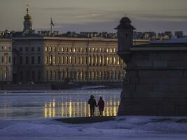 Evening view from the Neva river to Peter and Paul Fortress, Russia, Saint-Petersburg. Romantic couple in love walks along the embankment, a view from the back. City evening postcard view. photo