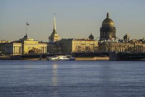 Tourist ship is sailing under the bridge. Spring St. Petersburg with a view of St. Isaac's Cathedral. View from the Neva River. Sunset view of the Palace Bridge, city life, postcard views. photo