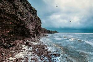 Rock cliff above the water with a tidal shoreline. Sea rocks cliffs in the ocean. Beautiful sea wallpaper for tourism and advertising. Stormy landscape. photo