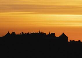 contrastando ver de oscuro silueta de el techos en contra el brillante naranja noche cielo. bajo ángulo ver de largo fila de característica casas adosadas con techos y chimeneas de Europa casas durante puesta de sol foto