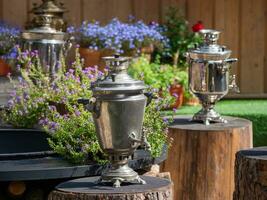 Silver samovars on old stump in outdoor, space for text. Russian tea culture. photo