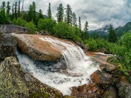 Cascades of a waterfall in a green mountain forest. Nature background of turbulent falling water stream on wet rocks. Taigishonok River, Western Sayans. photo