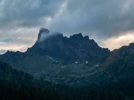 Dark atmospheric surreal landscape with dark rocky mountain top in low clouds. Gray low cloud on high pinnacle. High black rock  in low clouds. Surrealist gloomy mountains. West Saiyans. photo