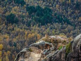 Minimalistic landscape of a rocky ledge against the background of a mountain forest. The edge of a stone cliff, a dangerous gorge. photo