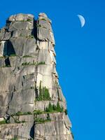 A large granite rock and a moon in the blue sky. Vertical view. photo