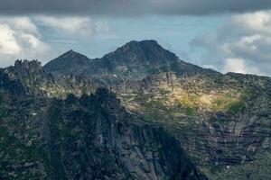 Sunlight glides along the slopes of majestic high and sharp mountains from each side. The peaks are shrouded in rainy haze. Remote and isolated place. photo