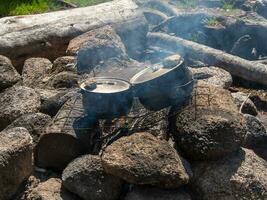 Camping kitchen. Cooking on a campfire in the wild. Two soot-covered kettles stand over the fire. Survival in the wild. Wonderful flame with calderon. Pots in the flames of the fire. photo