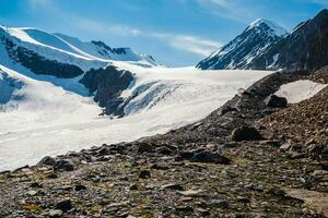 The way to the Aktru glacier. Snowy high-altitude plateau. Alpine landscape with snow-capped mountain peak and sharp rocks under blue sky. Colorful sunny mountain scenery with snow mountain top. photo