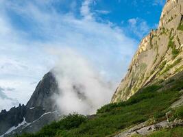 Sunrise in the mountains, in thick clouds. Light on the pass. The glacier is melting, illuminated by the bright golden morning sun. Fog on sunny slopes, natural majestic view. photo