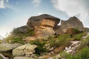 soleado tierras altas paisaje con grande piedras de raro forma. increíble escénico montaña paisaje con grande agrietado piedras de cerca entre césped debajo azul cielo en luz de sol. foto